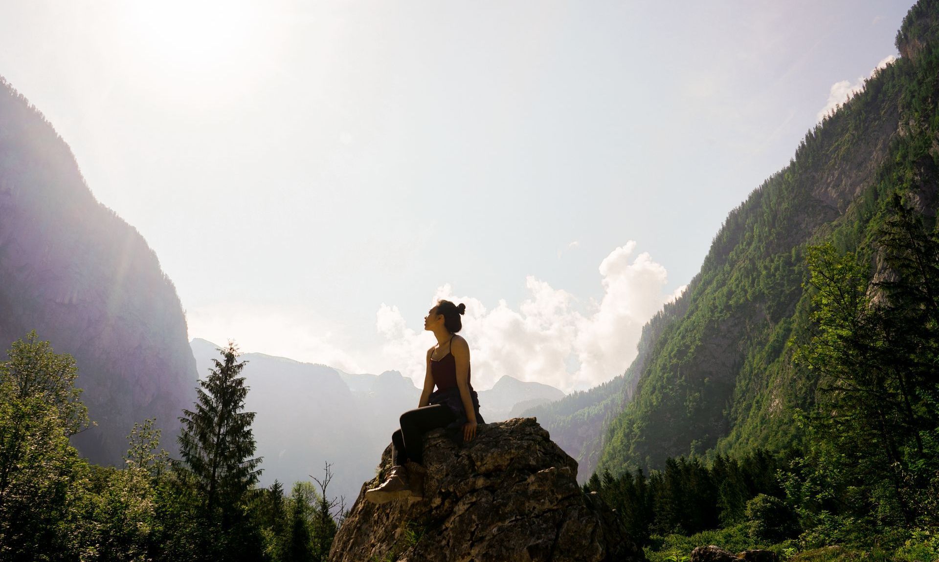 A woman is sitting on top of a rock in the mountains.
