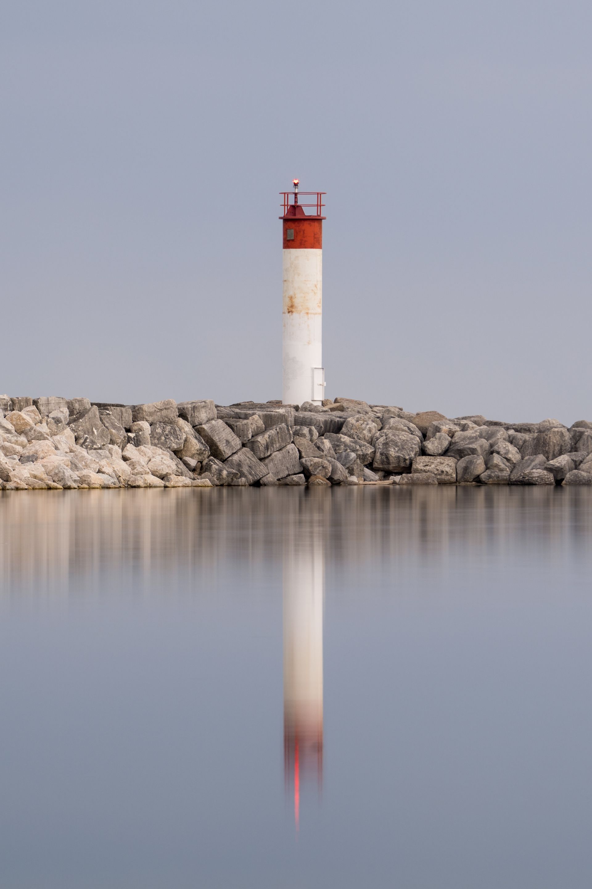 A red and white lighthouse is reflected in the water