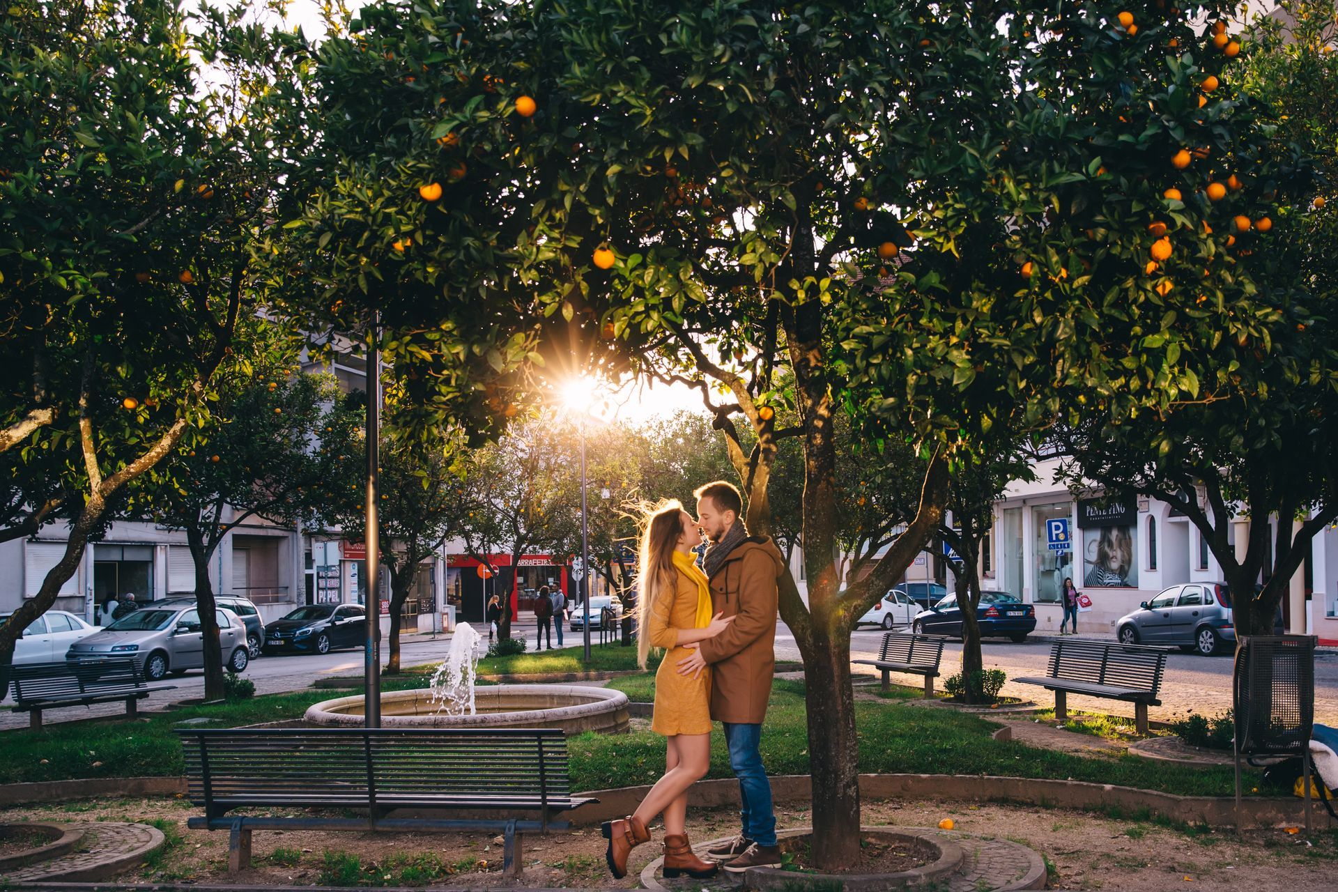 A man and a woman are kissing under a tree in a park.