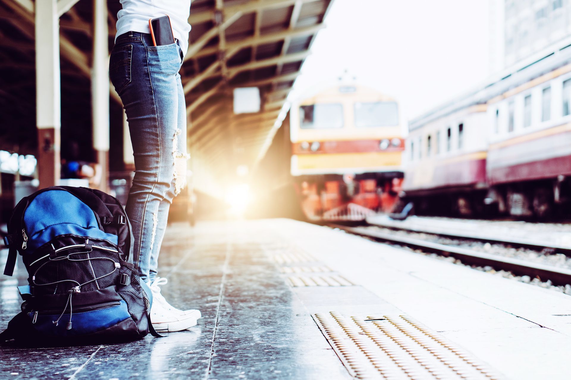 A woman is standing at a train station with a backpack.