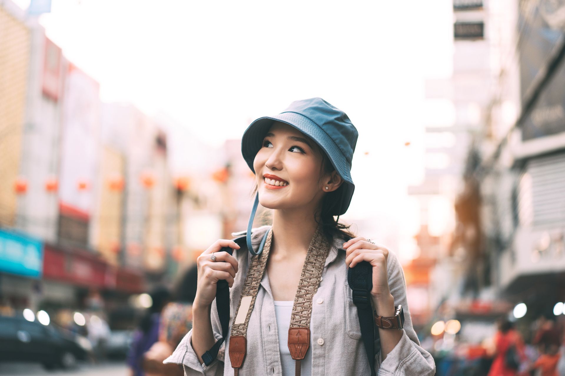 A woman wearing a hat and a backpack is walking down a city street.