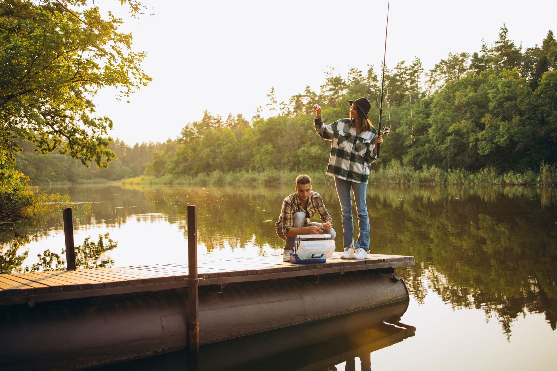 A man and a woman are fishing from a dock on a lake.