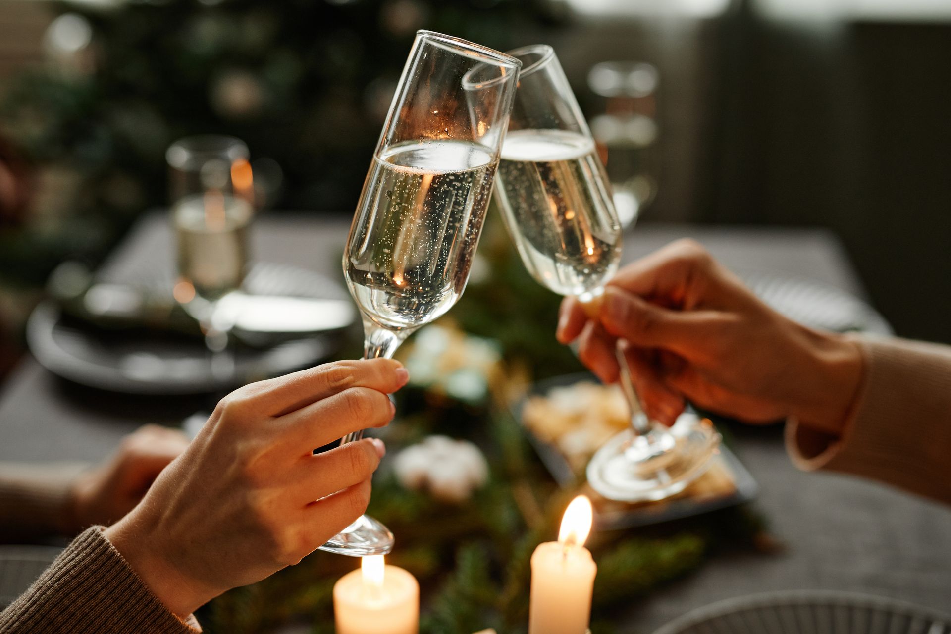 Two hands clink champagne flutes during a celebration at a candlelit table.