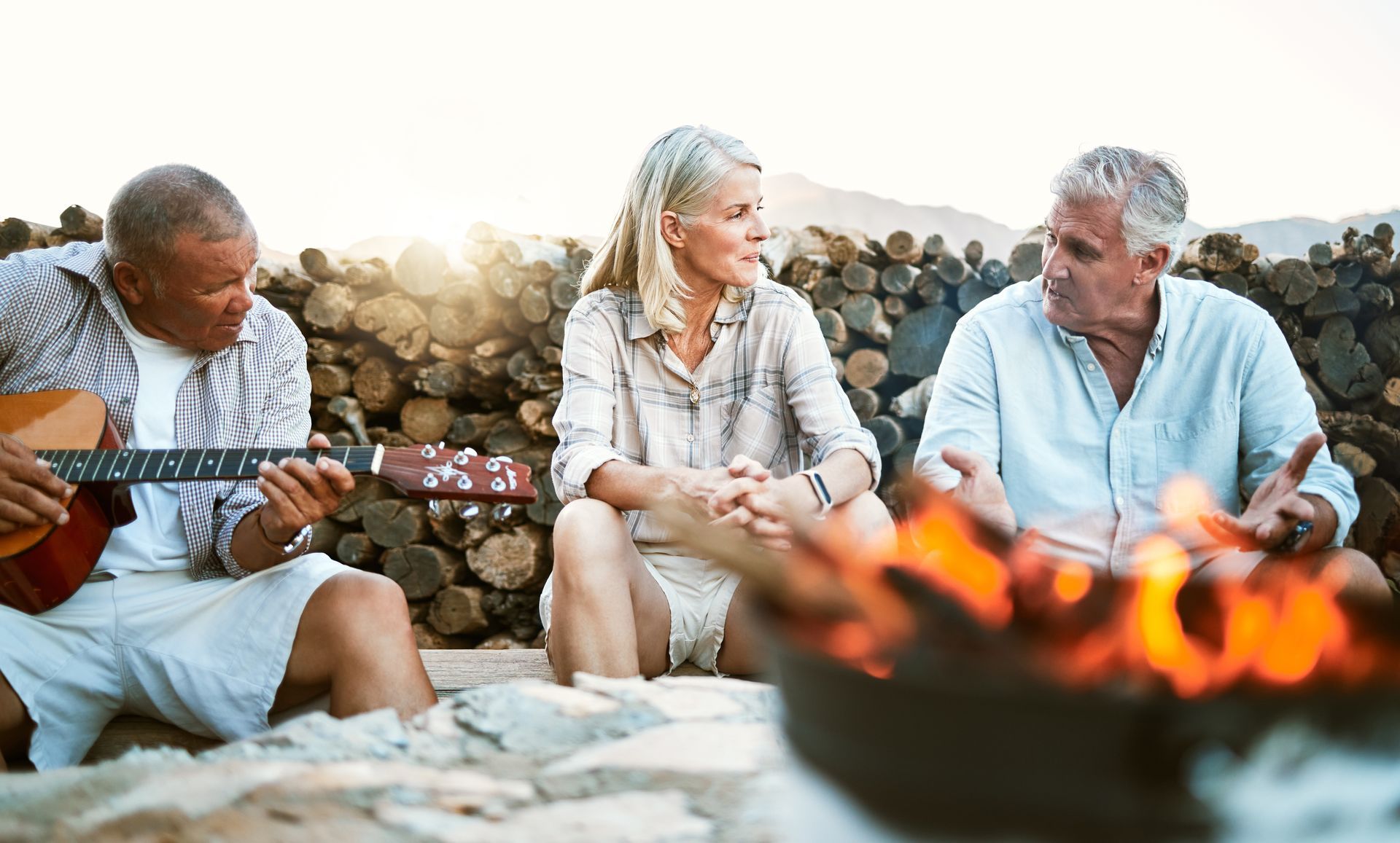 A group of people are sitting around a campfire while a man plays a guitar.