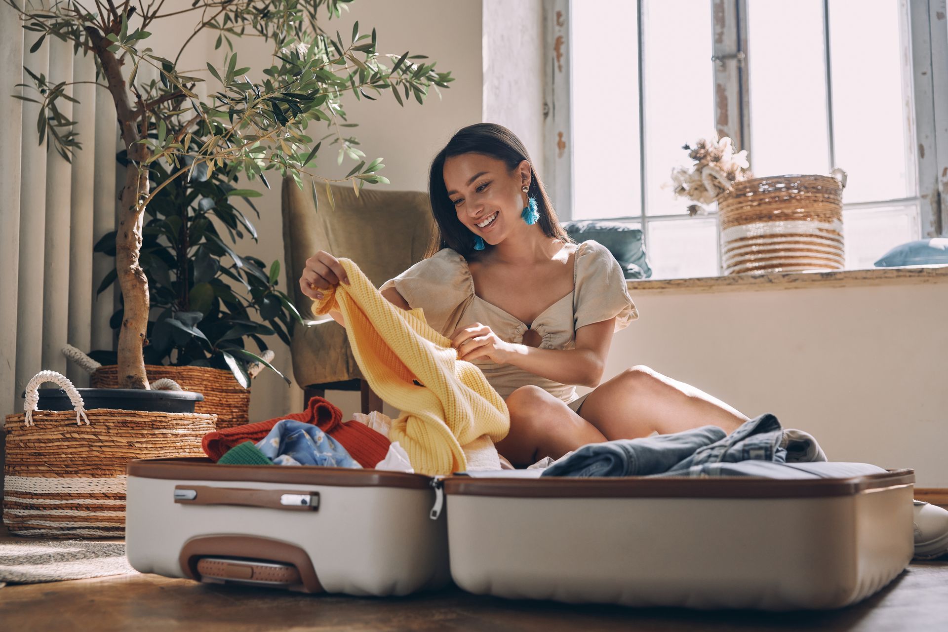 A woman is sitting on the floor packing a suitcase.