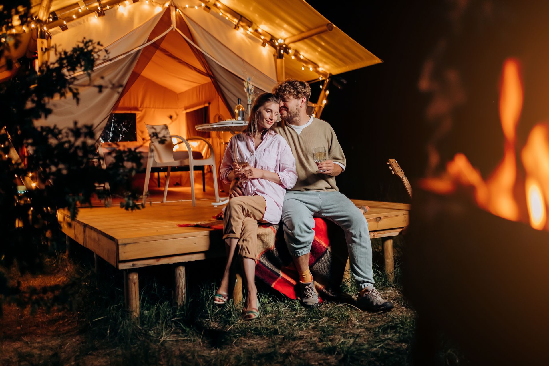 A man and a woman are sitting on a deck in front of a tent.