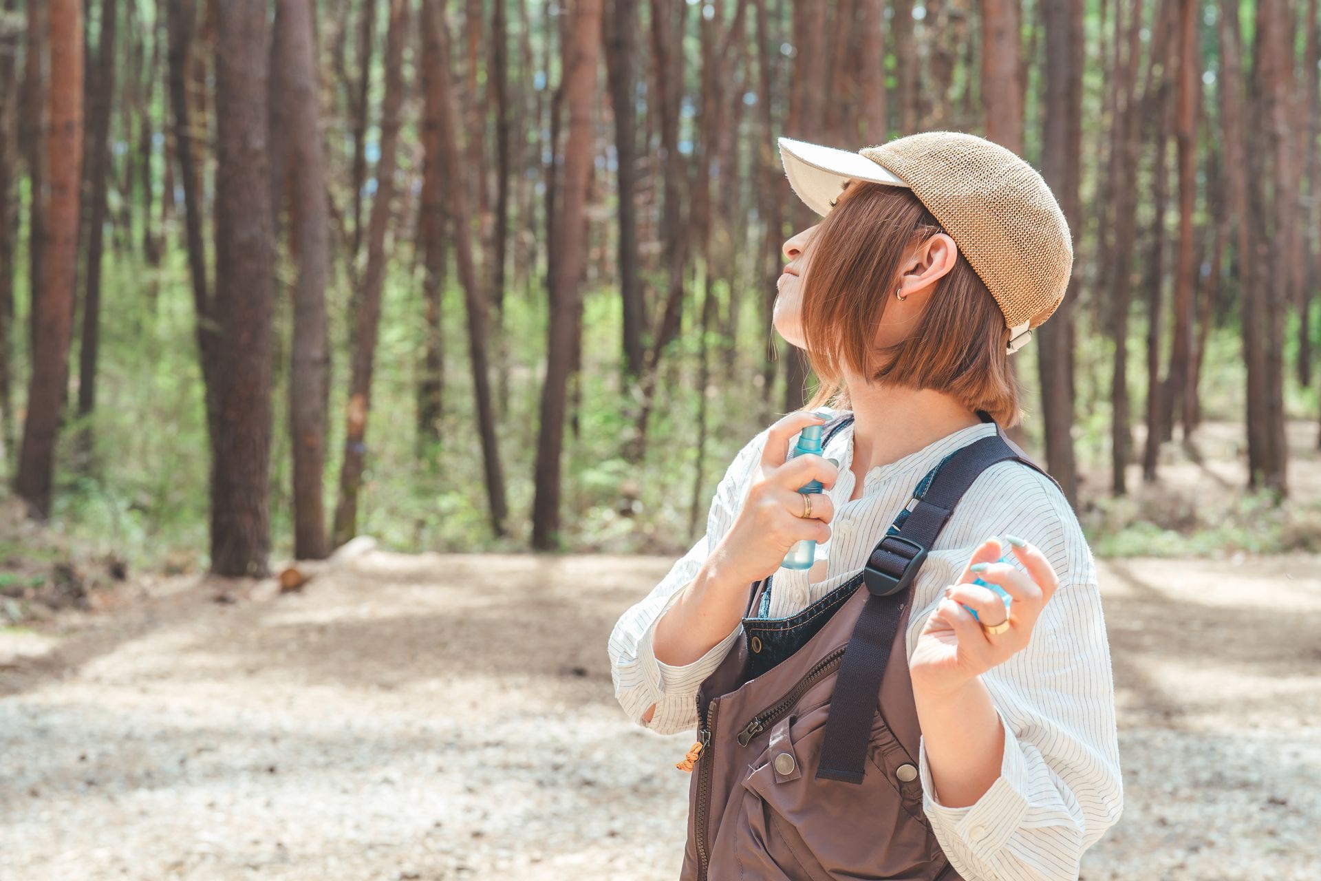 A woman is spraying perfume on her neck in the woods.