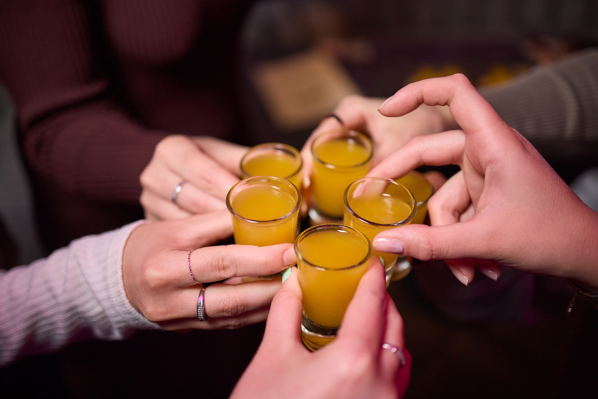 Hands toasting with six cider shots.