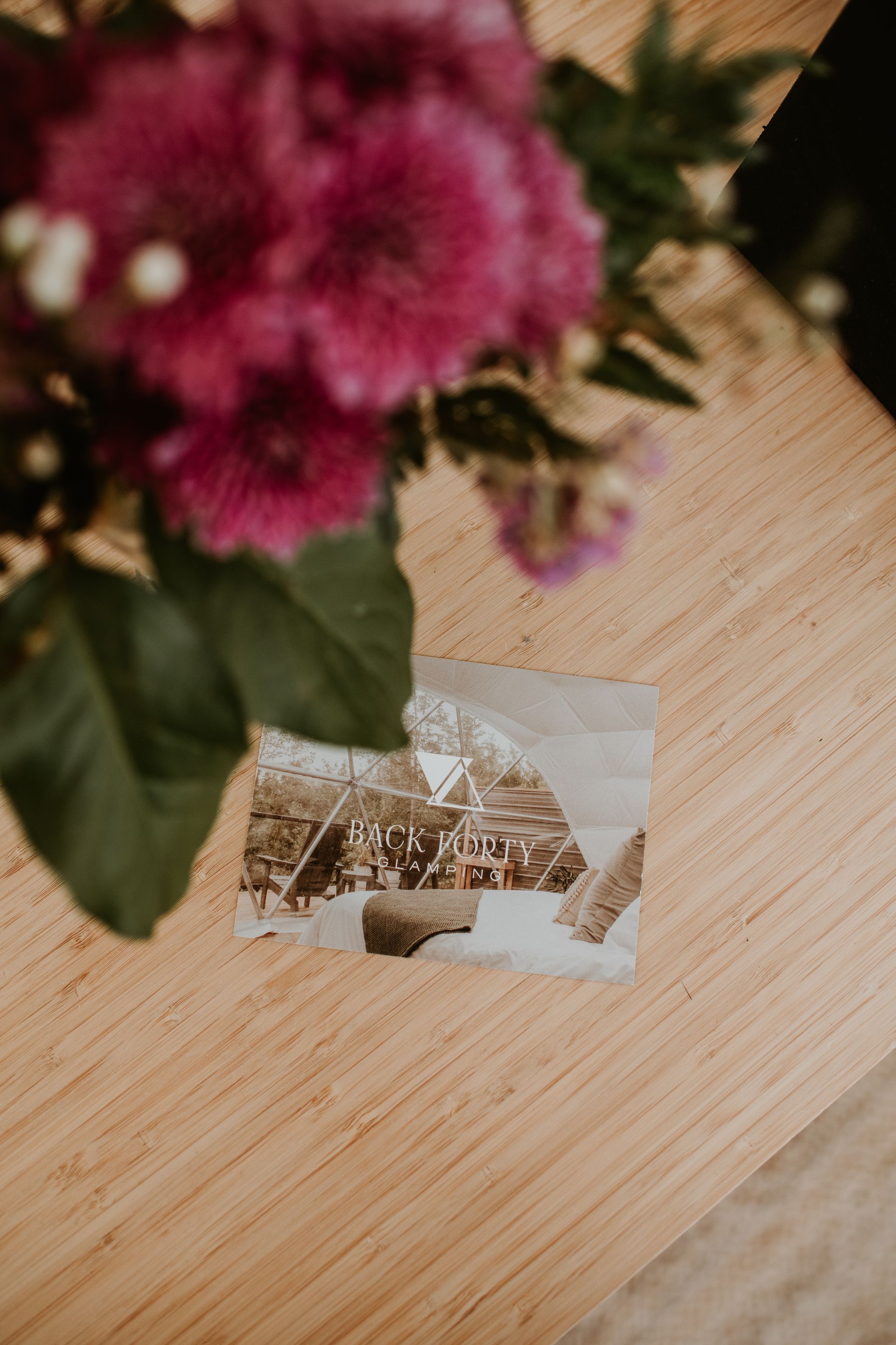 A picture of a house is sitting on a wooden table next to a bouquet of flowers.