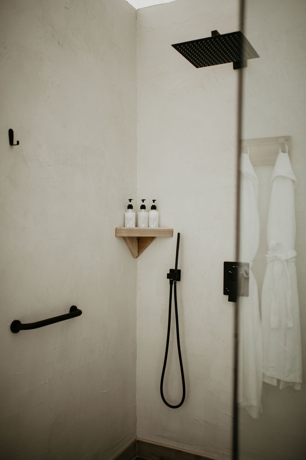 A shower with a black shower head and a shelf with bottles on it.