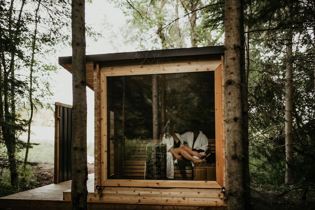 A man is sitting in a wooden sauna in the woods.
