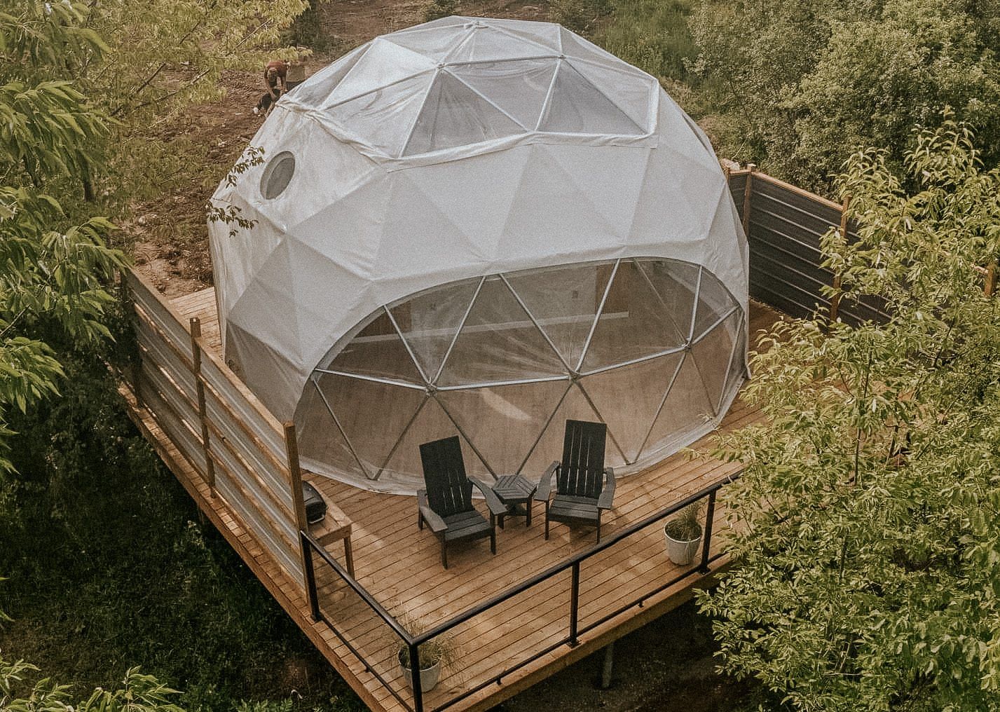 An aerial view of a dome tent on a wooden deck surrounded by trees.