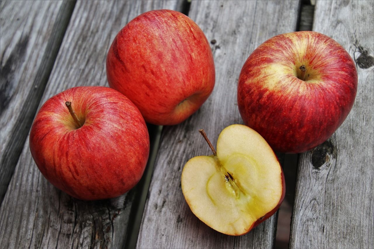 Three apples are sitting on a wooden table with one apple cut in half.