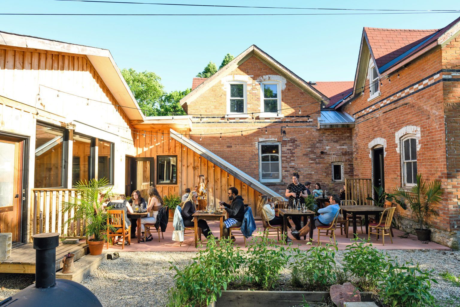 A group of people are sitting at tables outside of a brick building.