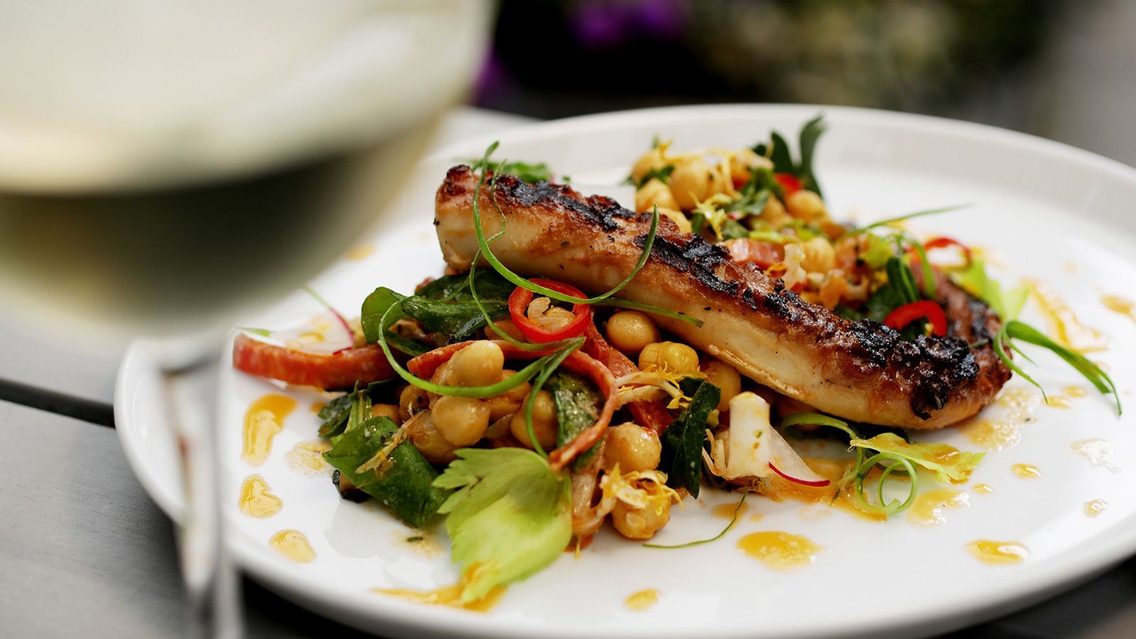A white plate topped with meat and vegetables next to a glass of wine.