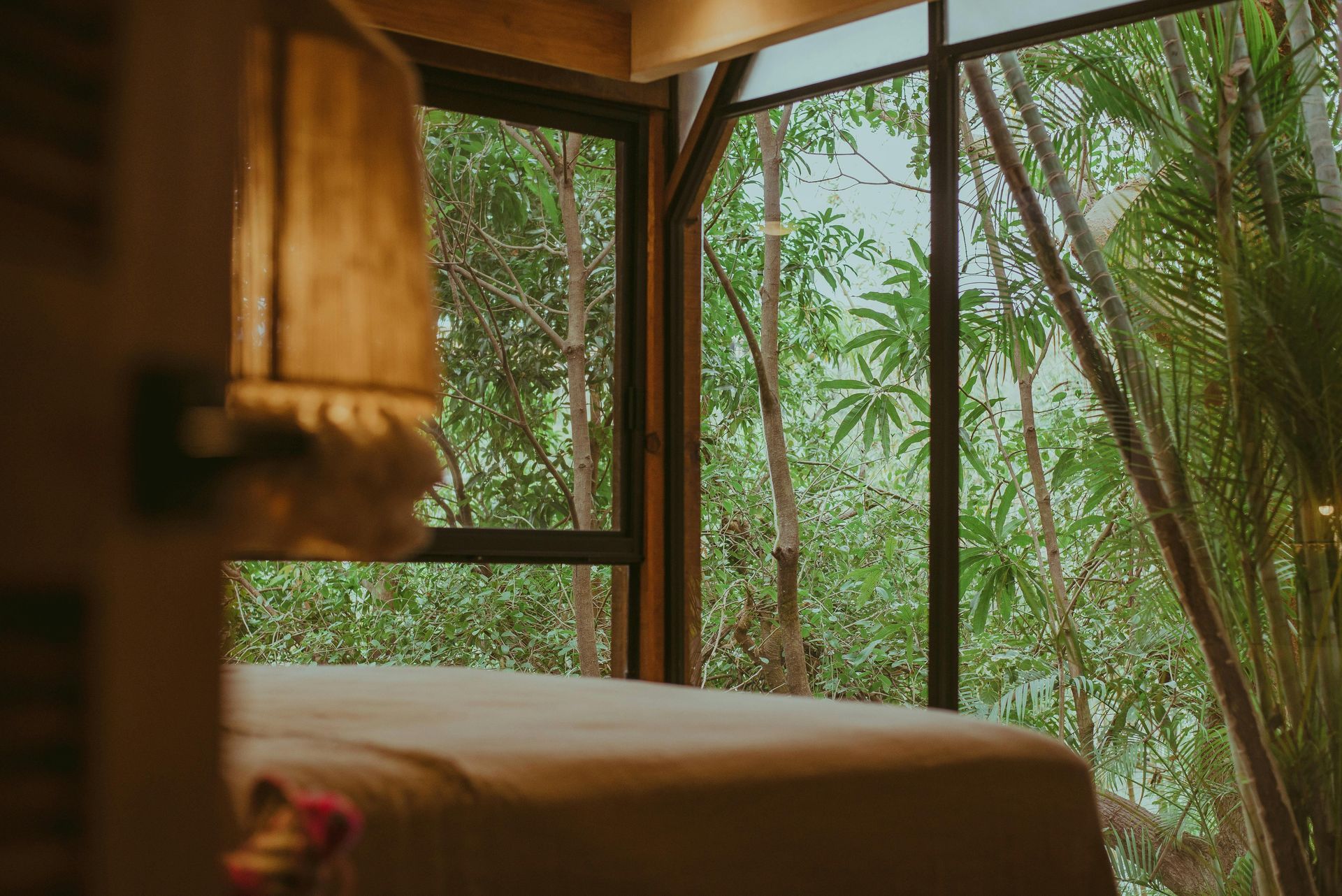 Bed in a cabin with large windows overlooking lush green trees.
