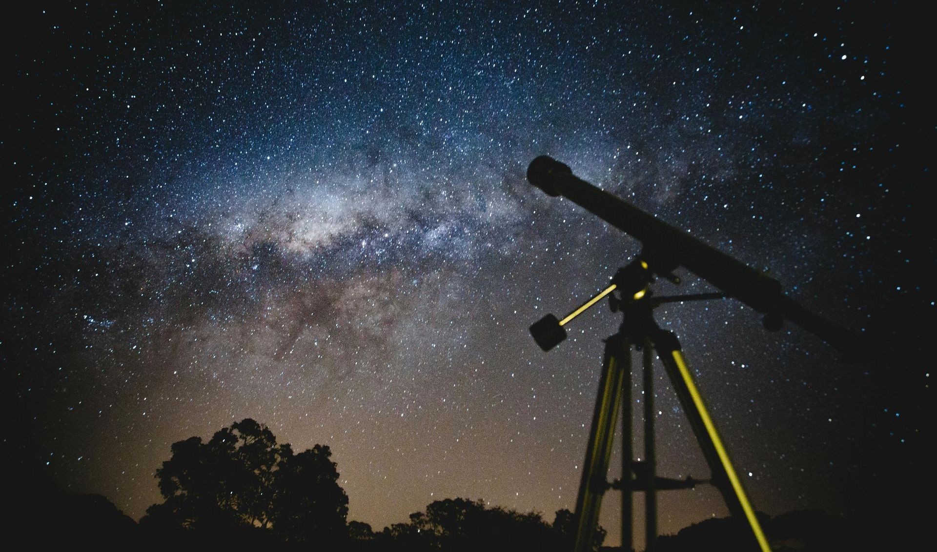 A telescope is sitting on a tripod under a starry night sky.