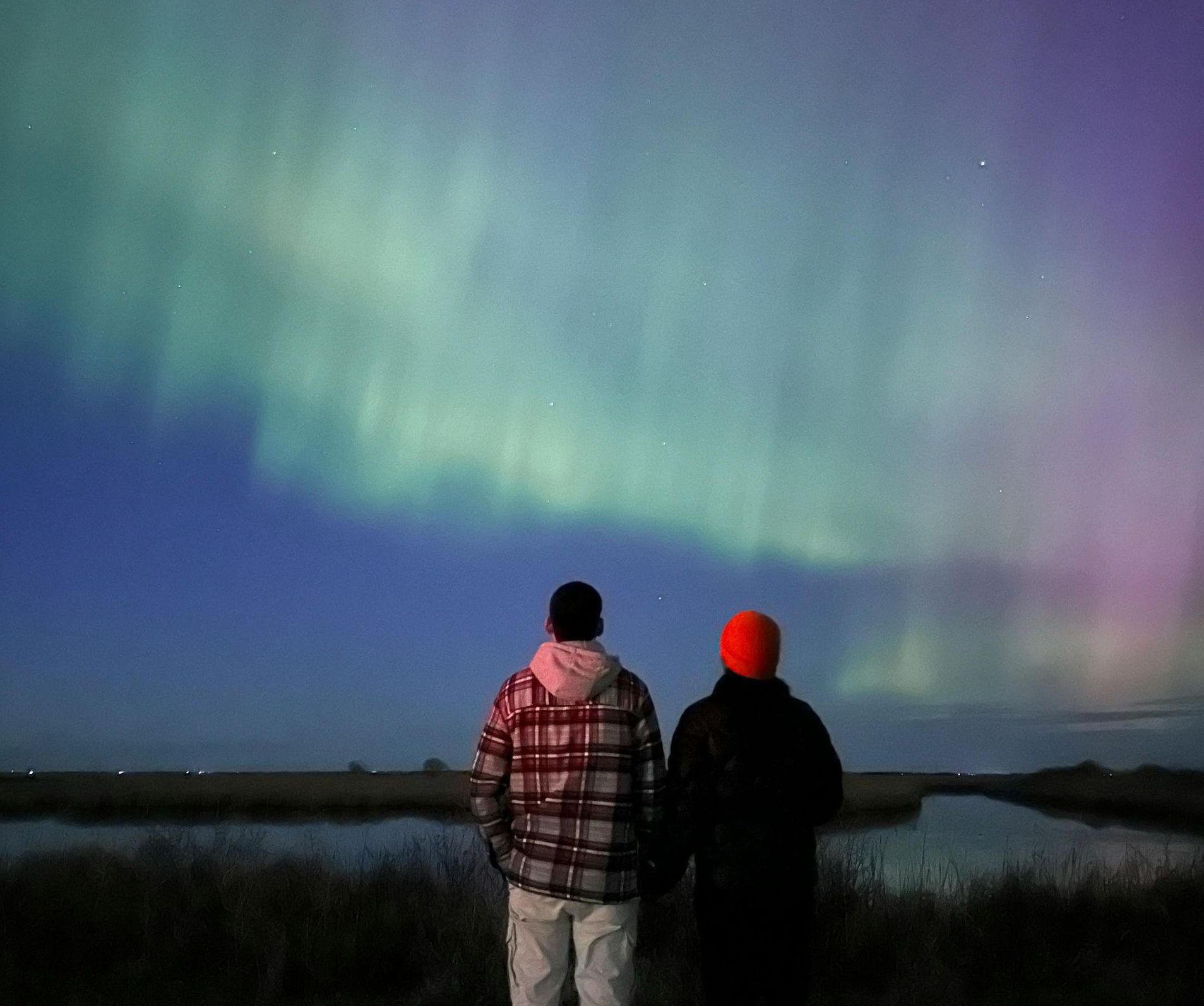 Two people are looking at the aurora borealis over a body of water.