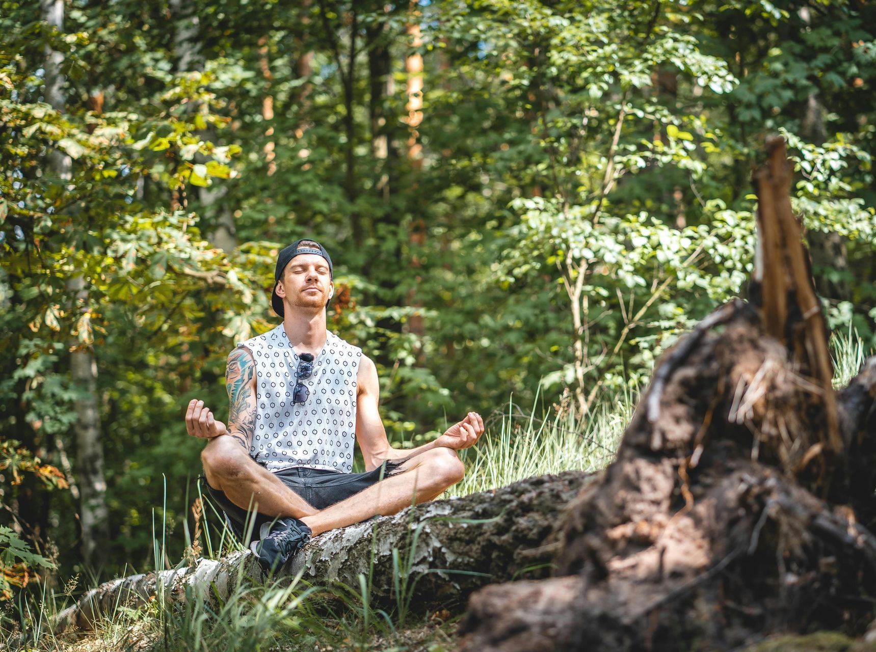 A man is sitting in a lotus position on a log in the woods.