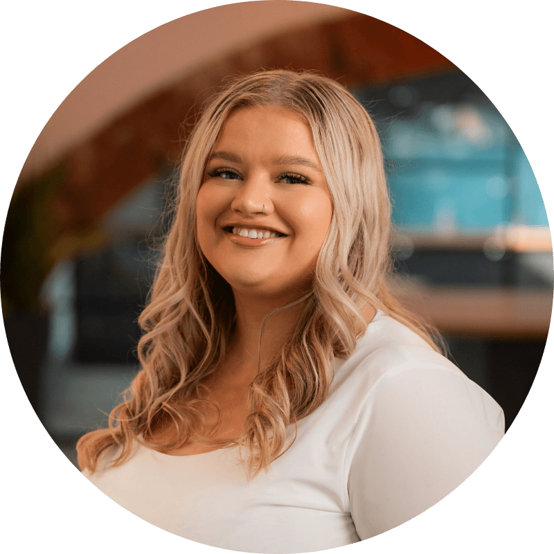 Woman with blonde hair smiles, wearing a white shirt in an indoor setting.