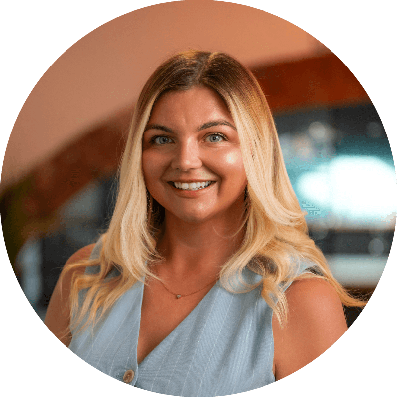 Woman with blonde hair smiling, wearing a light blue top, indoors.