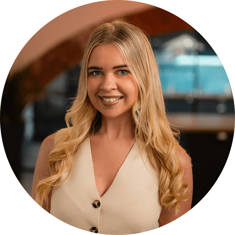 Blonde woman smiling, wearing a cream top with buttons, indoors.