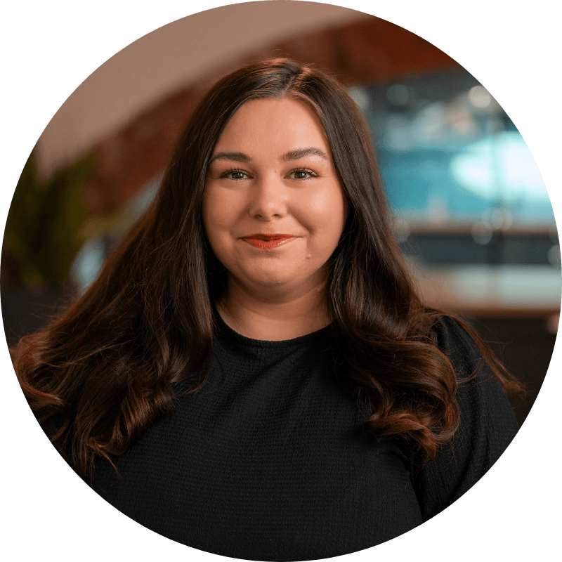 Woman with long brown hair, smiling, wearing a black top, in an office setting.