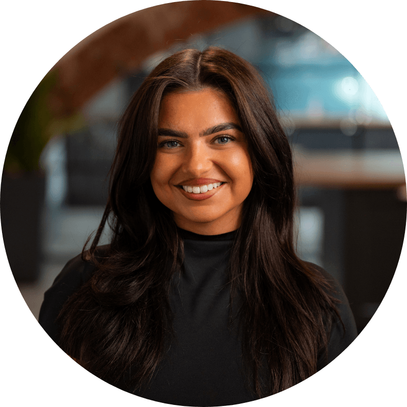 Woman with dark hair smiling at the camera in a modern office setting.