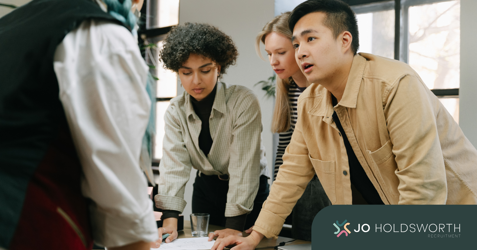 People leaning over a table in a bright office, collaborating in a discussion.