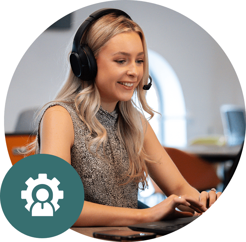 Woman with headset smiles while using a laptop. Office setting, gear icon.