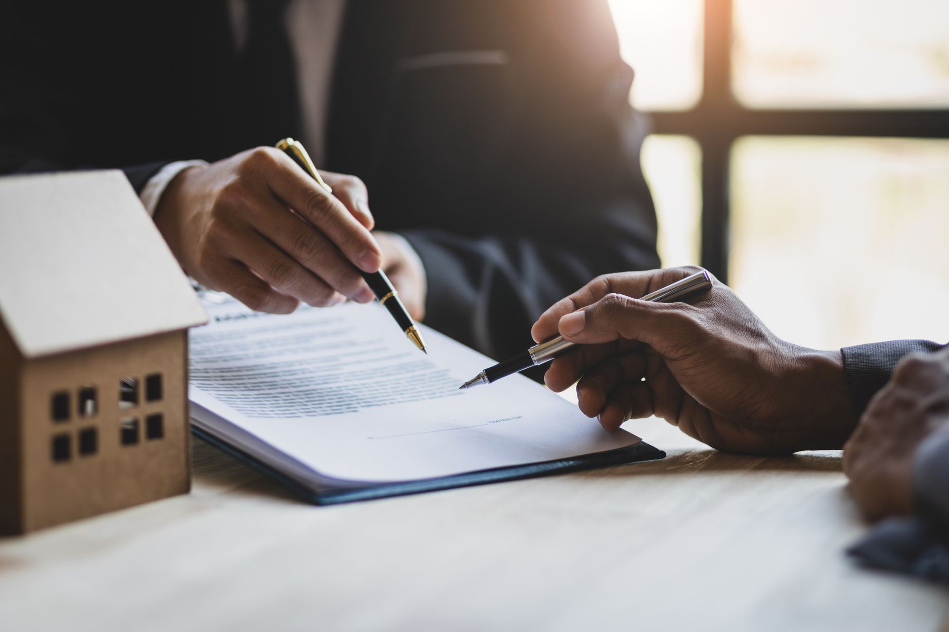 Two people signing a real estate contract, miniature house model on the table.