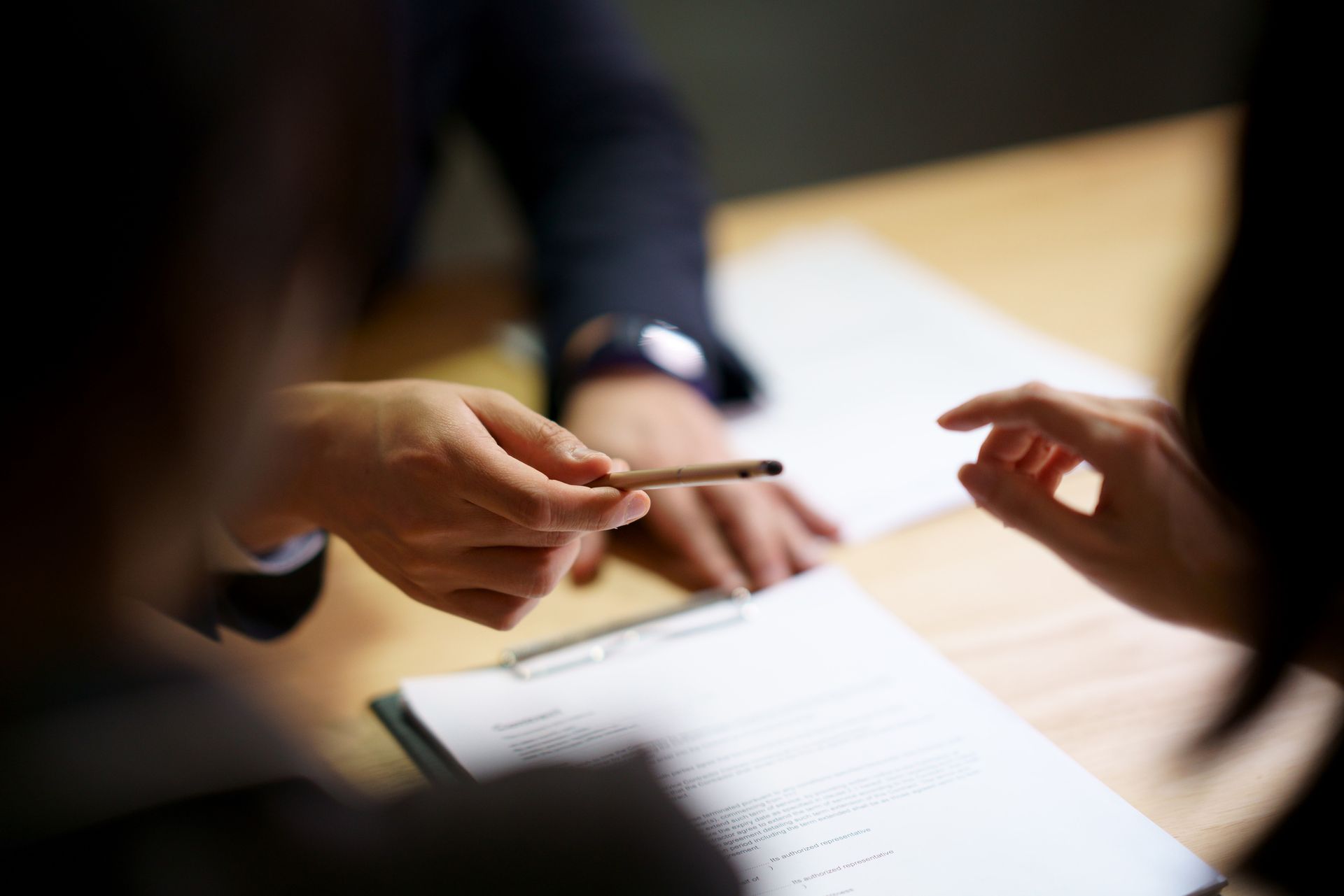 Hands holding a pen and pointing at a document during a meeting.