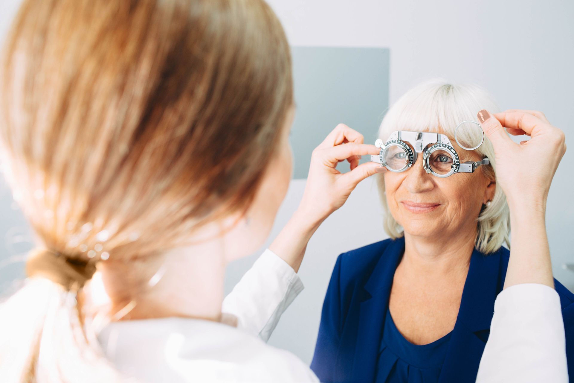 Optician fitting red eyeglasses on a smiling woman in an eye clinic.