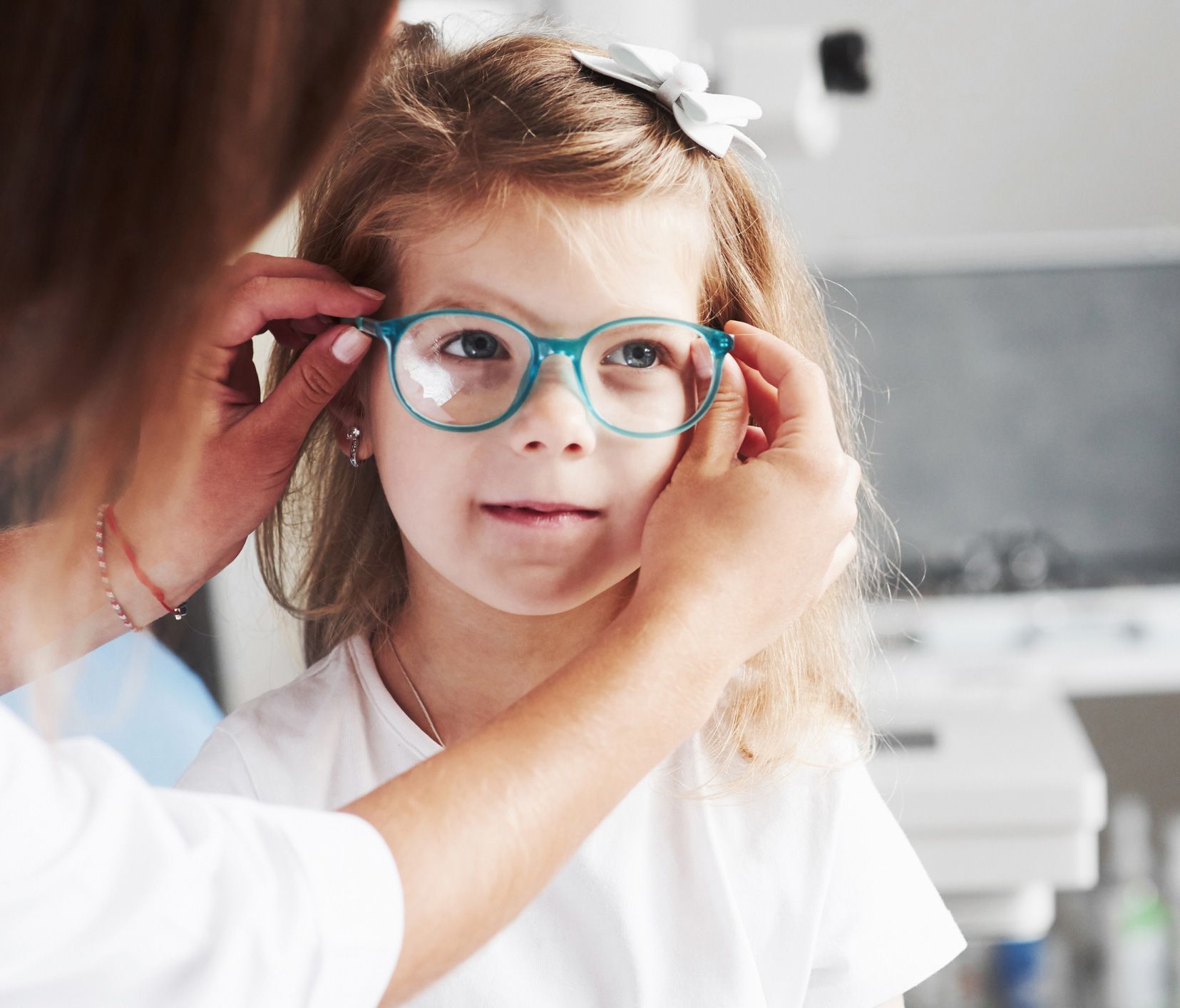 Woman adjusting eyeglasses on a young girl in an eye doctor's office.