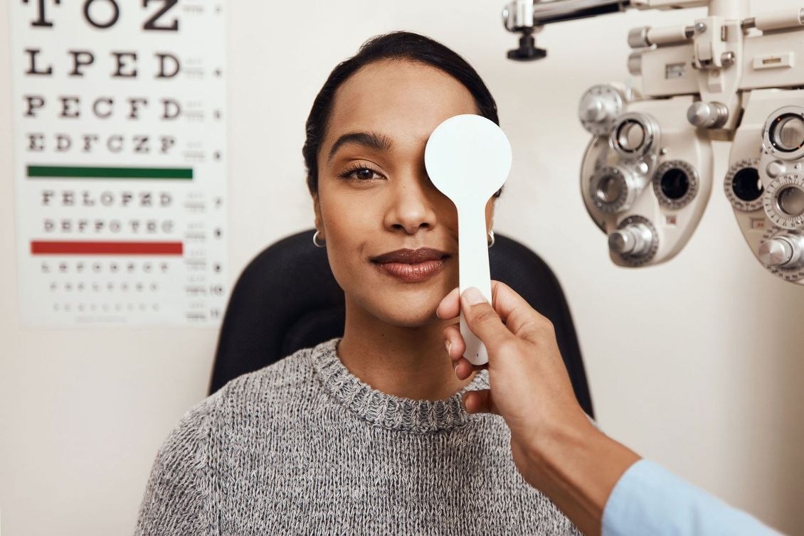 Woman during eye exam, covering one eye with a paddle, looking at chart.