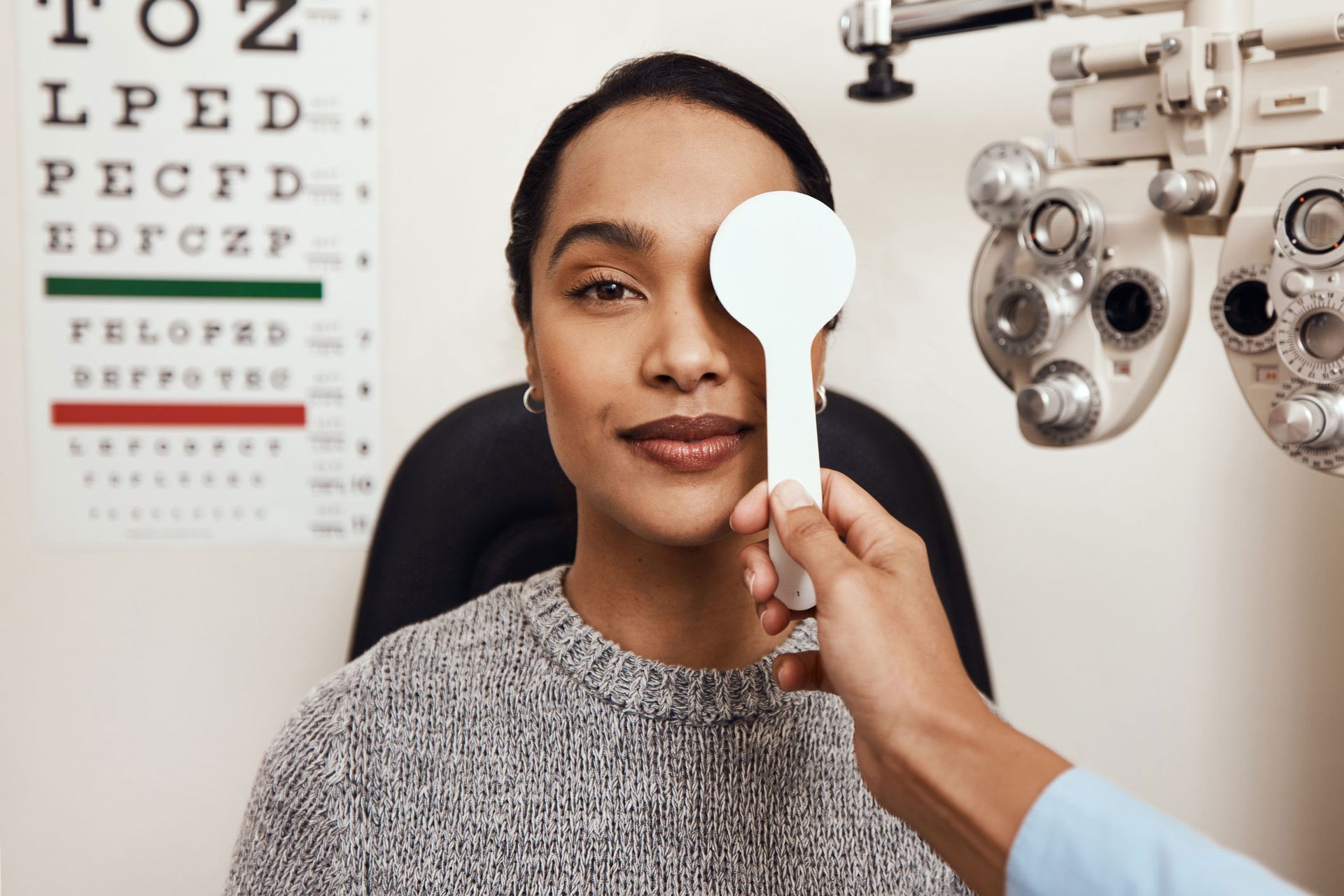 Woman during eye exam, covering one eye with a paddle, looking at chart.