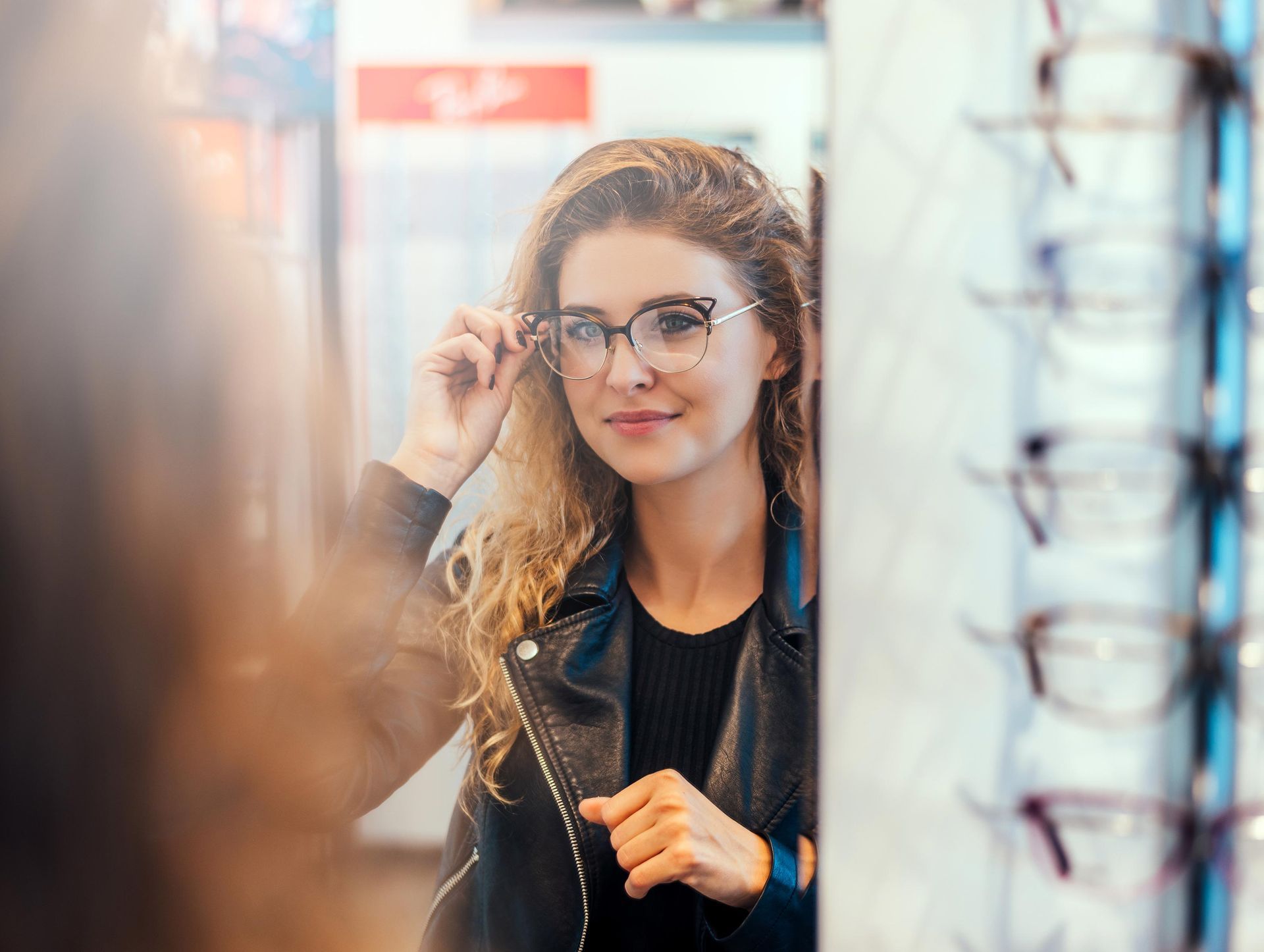 Woman in glasses looking in a mirror, trying on eyewear in a shop.