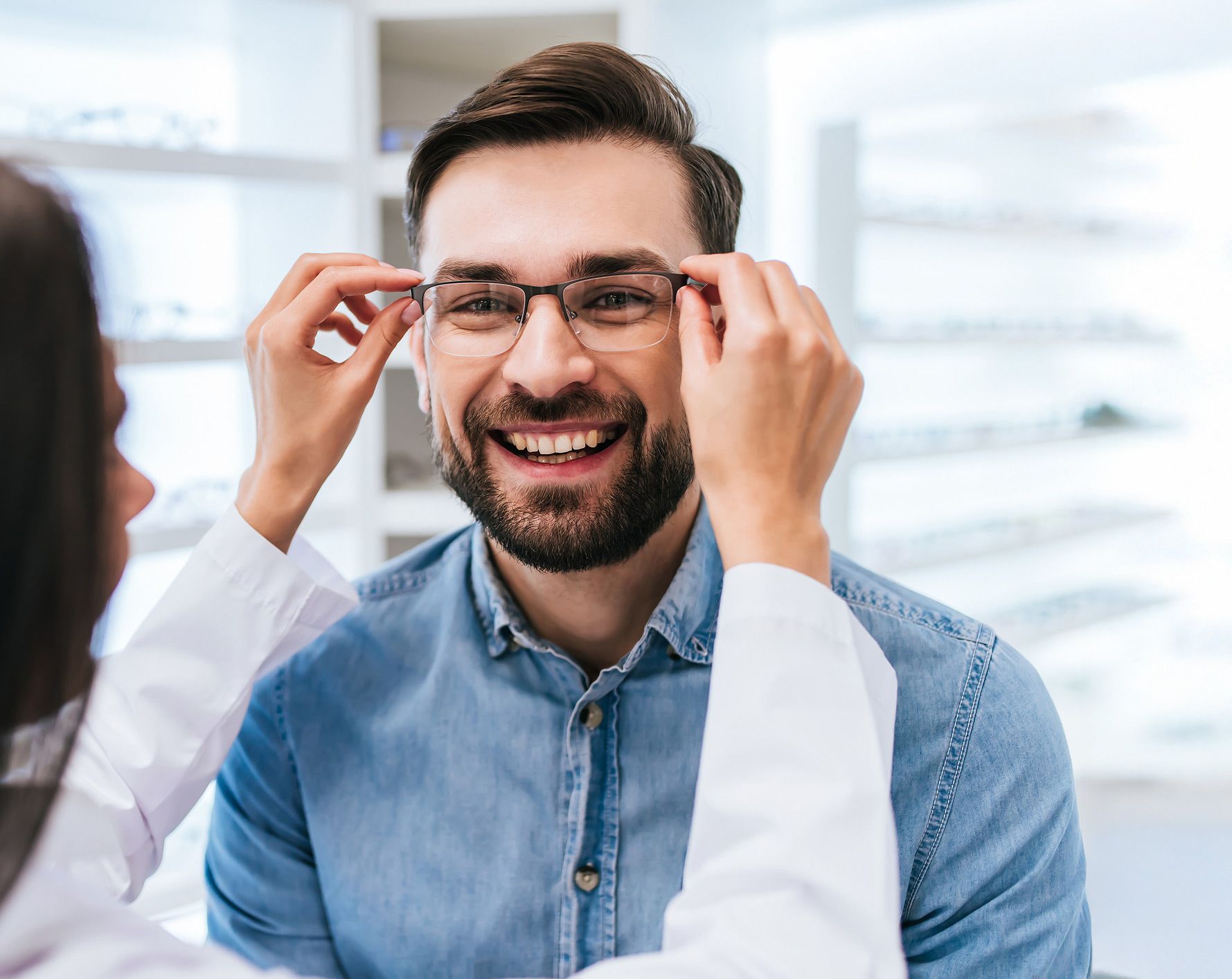 Man smiling as an optician adjusts his new glasses in an optical store.