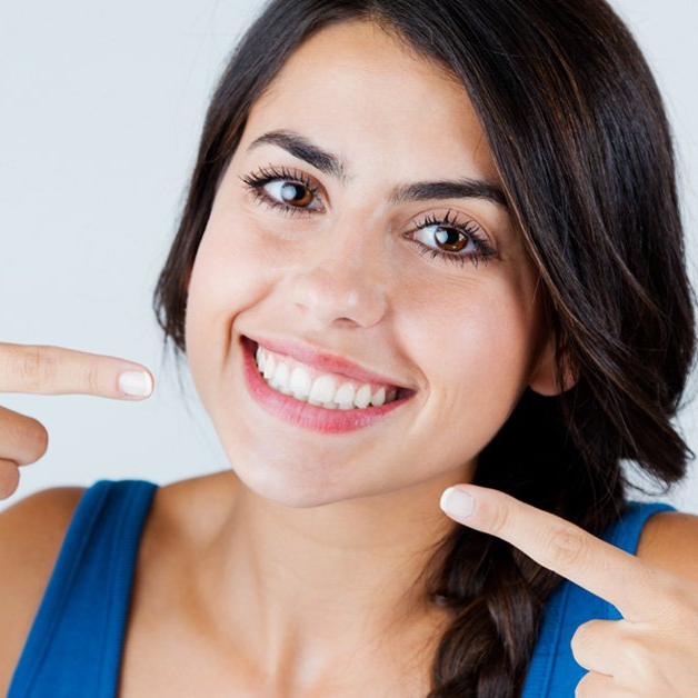 a woman in a blue tank top is smiling and pointing at her teeth