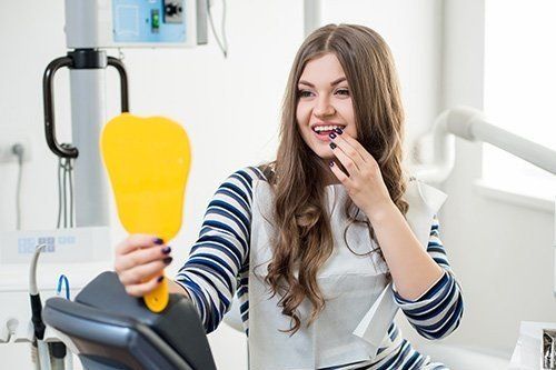 a woman is sitting in a dental chair looking at her teeth in a mirror .