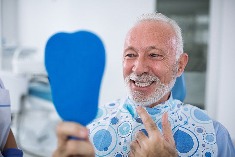 an older man is smiling while looking at his teeth in a mirror .