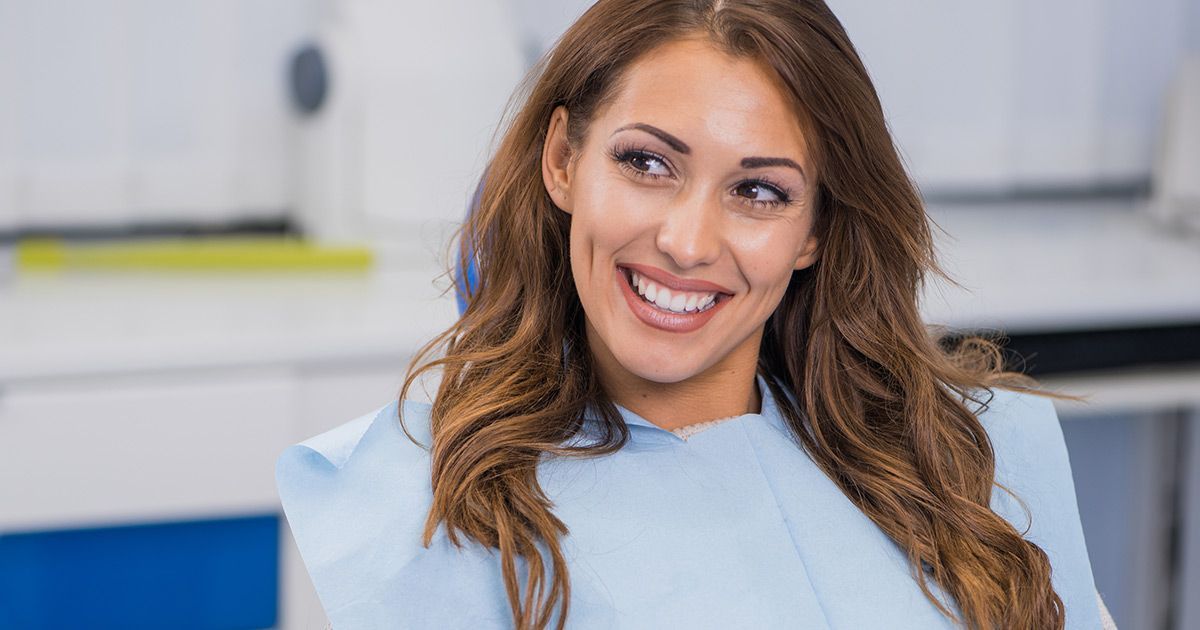 A woman is smiling while sitting in a dental chair.