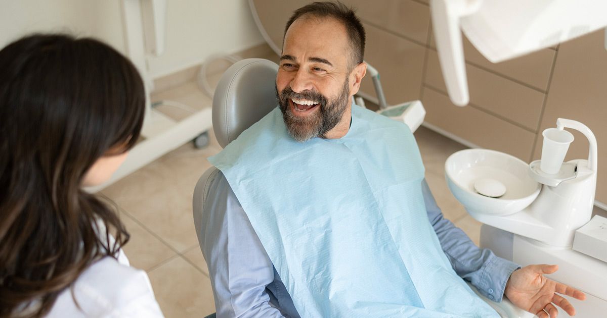 A man is sitting in a dental chair talking to a dentist