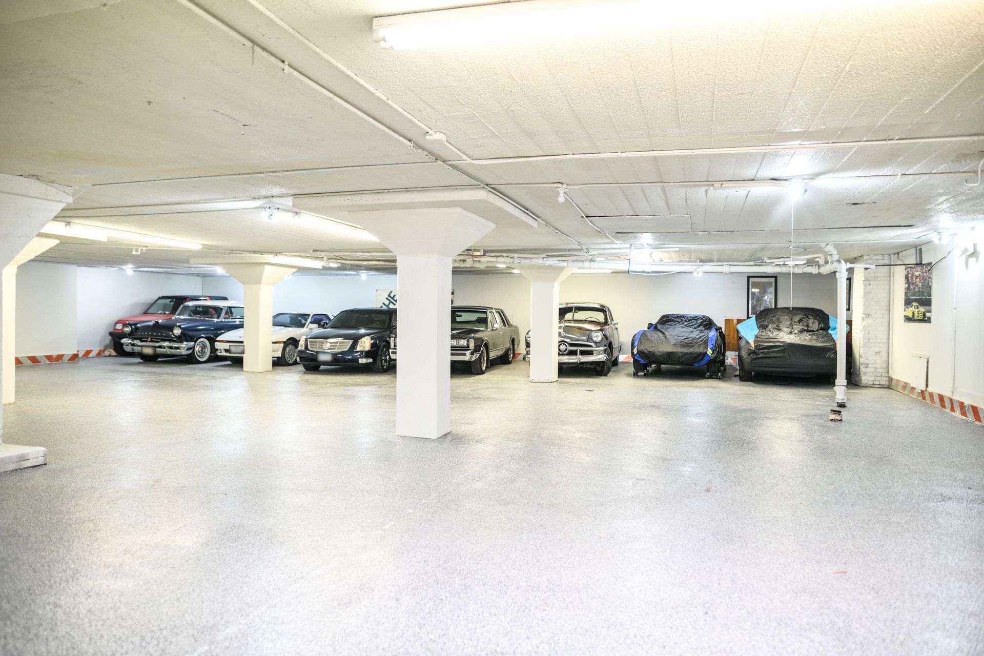 A large, brightly lit garage showcasing a collection of parked cars on a speckled floor. White columns and ceiling.