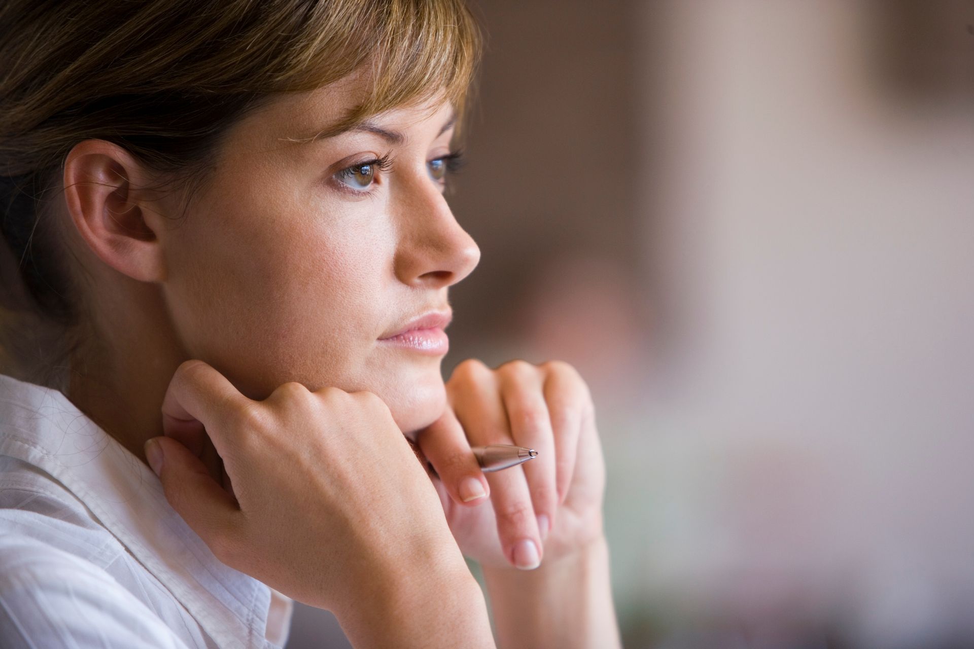 A person looking off-camera, resting their chin on their hands while holding a pen.
