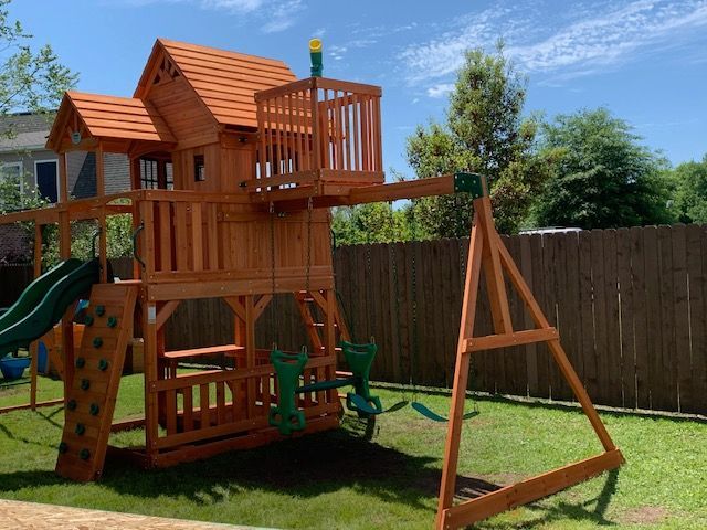 A wooden playground set in a backyard with a slide and swings.
