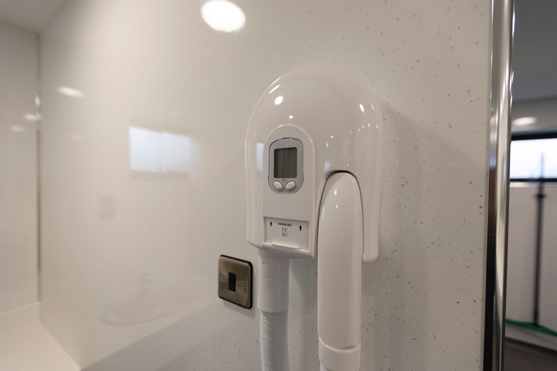 A white hair dryer is hanging on a white wall in a bathroom.