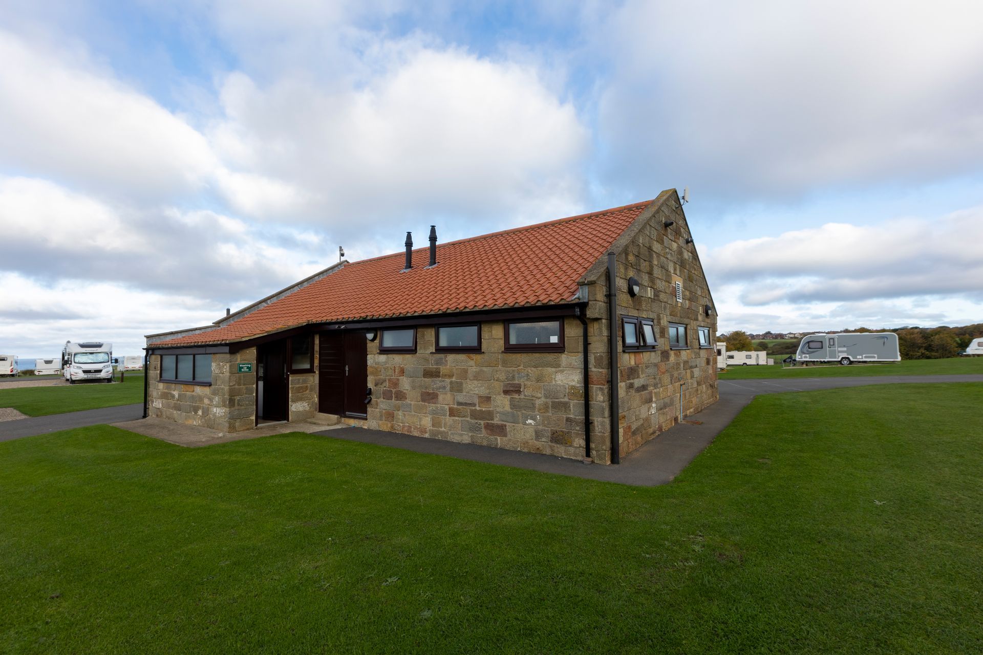 A small stone building with a red tile roof is sitting in the middle of a grassy field.
