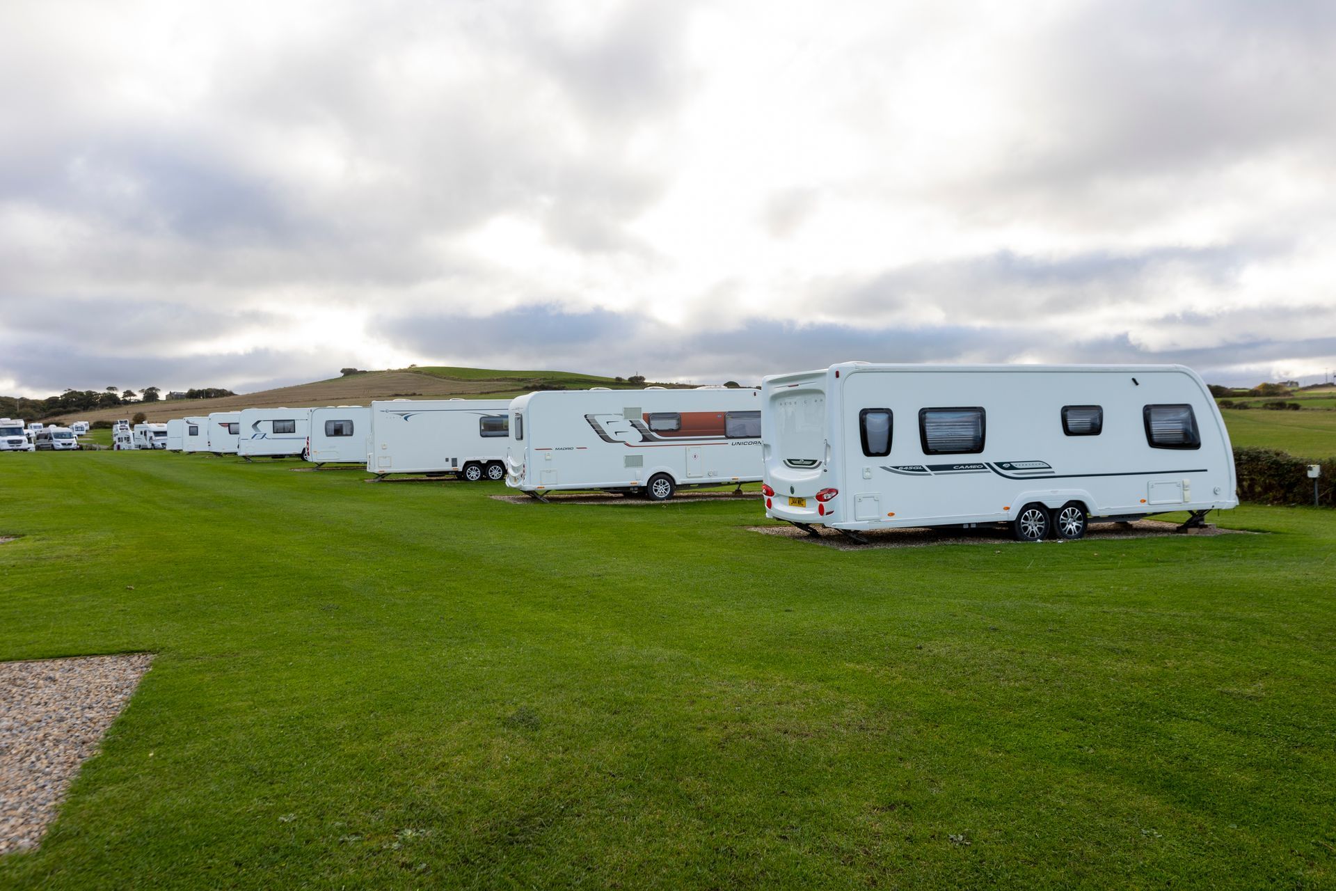 A row of caravans are parked in a grassy field.