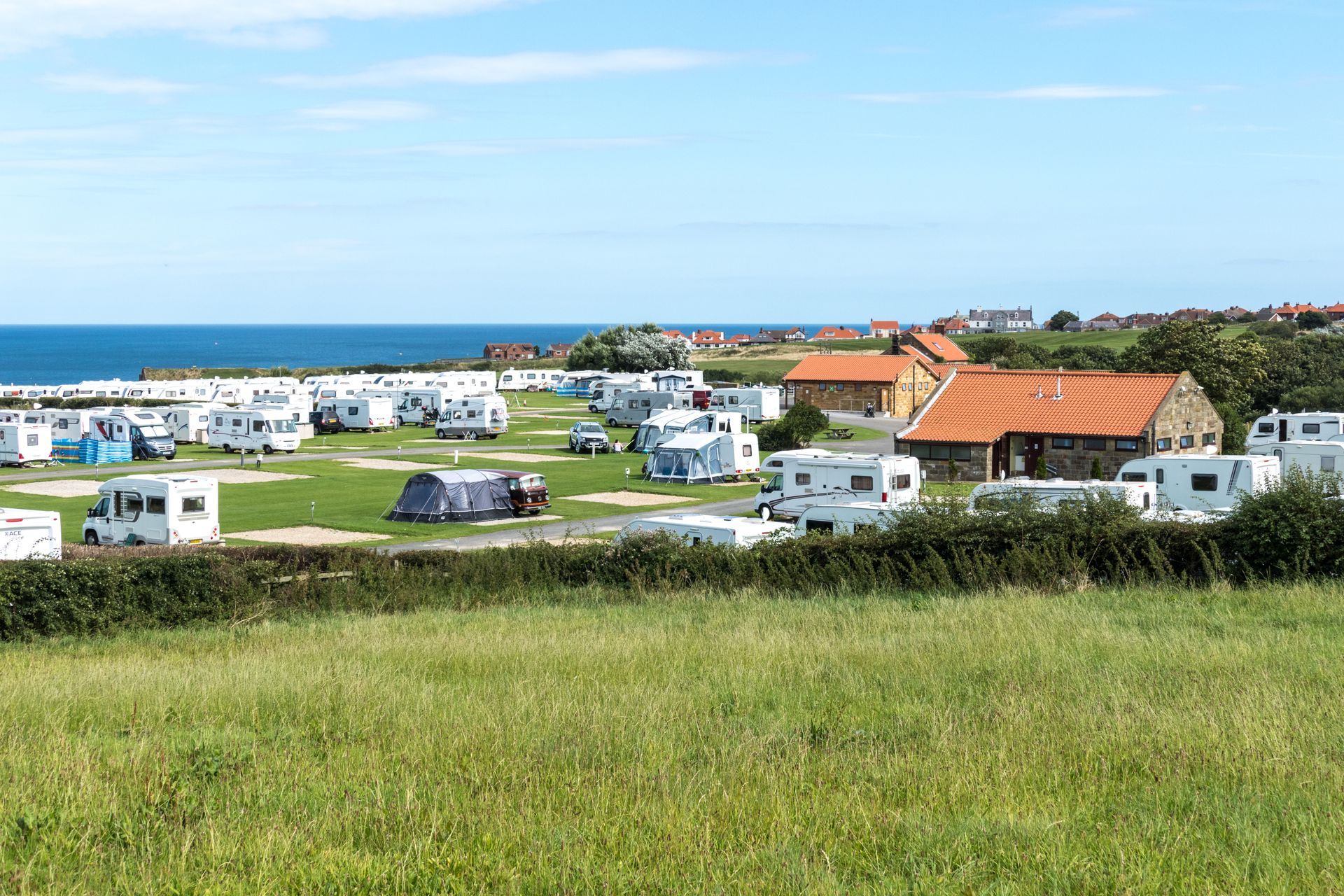 There are a lot of rvs parked in a field near the ocean.